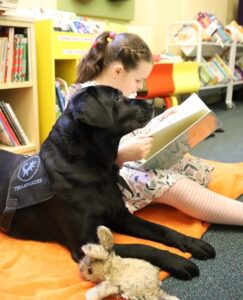 Tüdruk istub koos koeraga põrandal suure padja peal ja loeb raamatut.