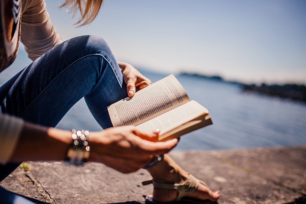 päikselisel suvepäeval loeb naine merelahe ääres kivist rinnatisel istudes raamatut