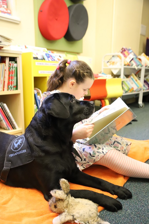 Esiplaanil must retriiver, tema kõrval istub raamatut lugev tüdruk.